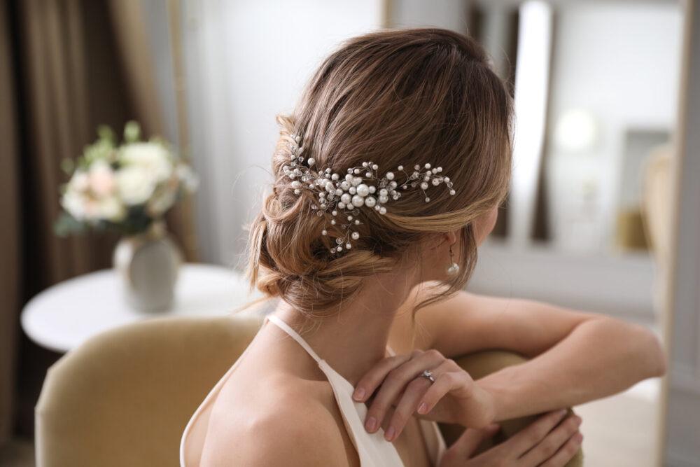 unge Braut mit eleganter Hochzeitsfrisur im Zimmer