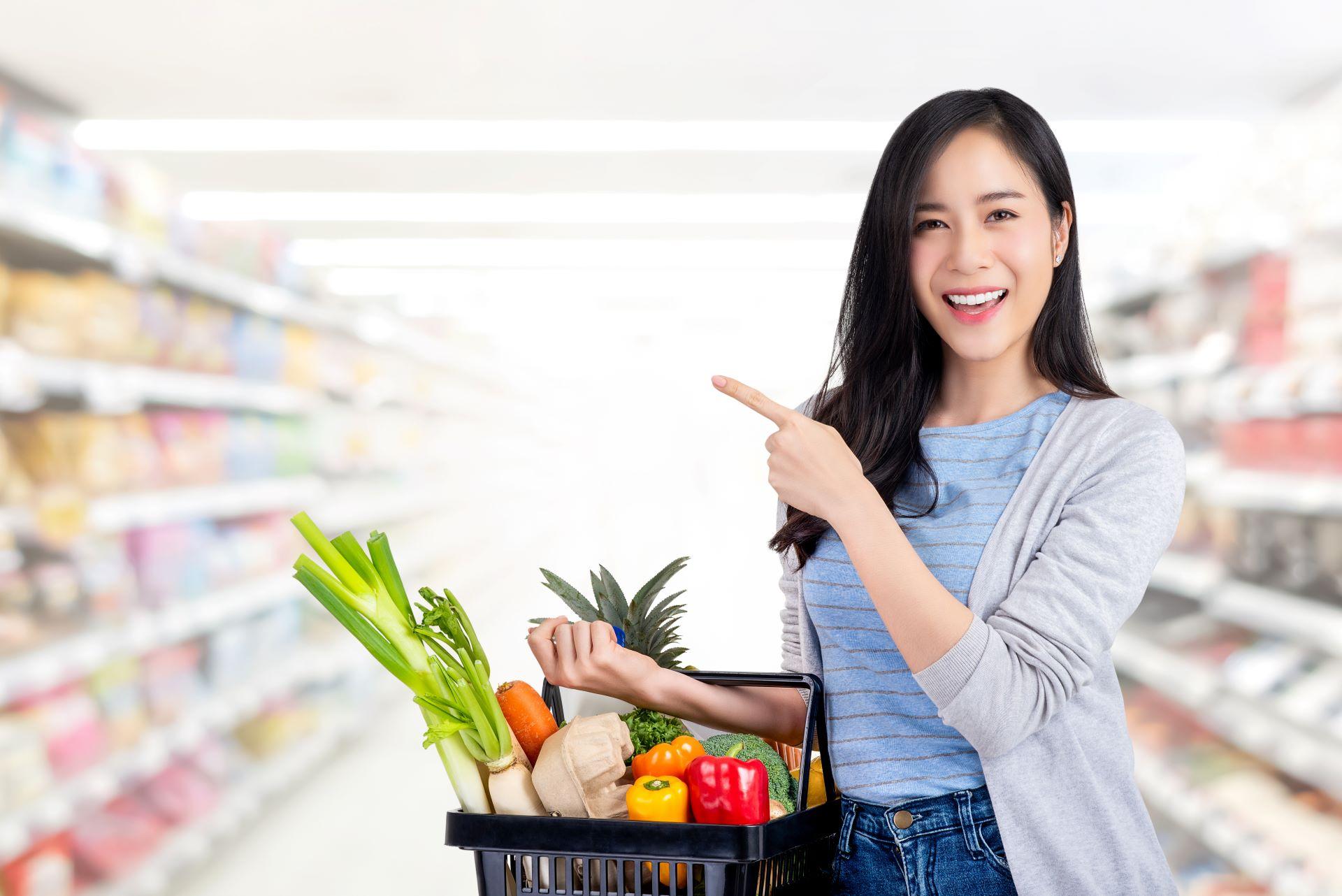 Asiatische Frau mit Einkaufskorb voller Lebensmittel im Supermarkt