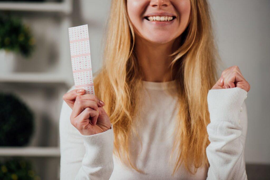 Lächelnde Frau hält einen Lottoschein und freut sich über Lotto 3 Richtige und einen kleinen Gewinn