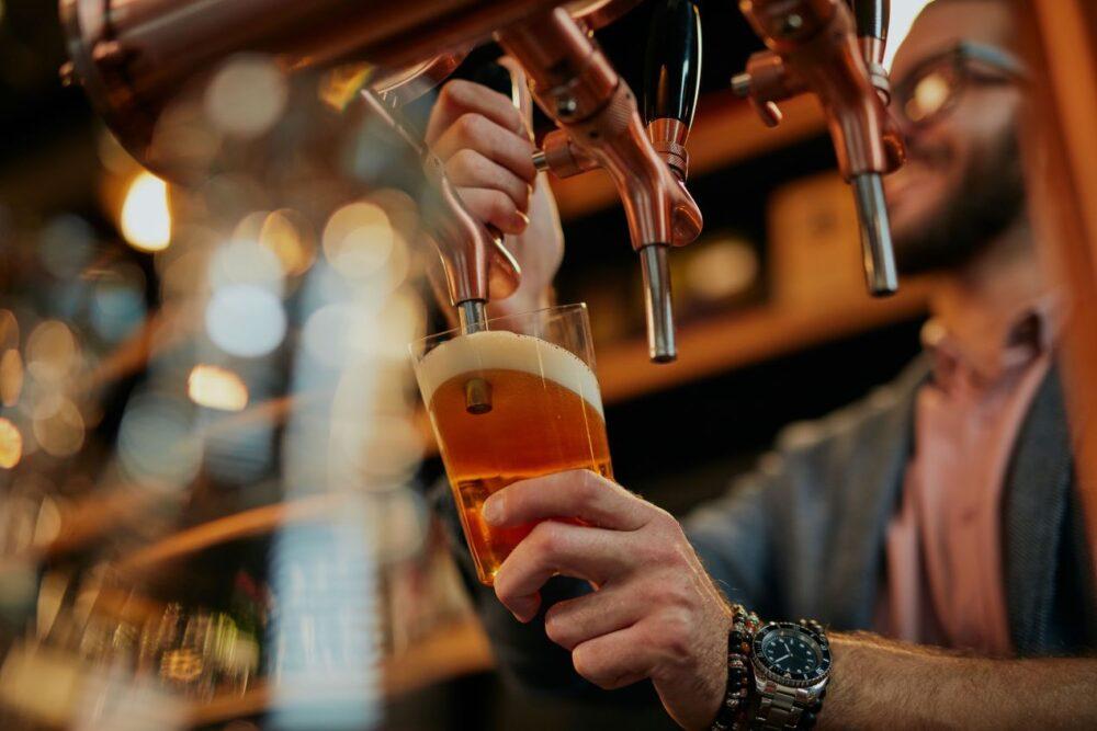 Ein Barkeeper zapft ein frisches IPA Bier in ein Glas. Das bernsteinfarbene Bier mit cremiger Schaumkrone symbolisiert den handwerklichen Craft-Beer-Trend.
