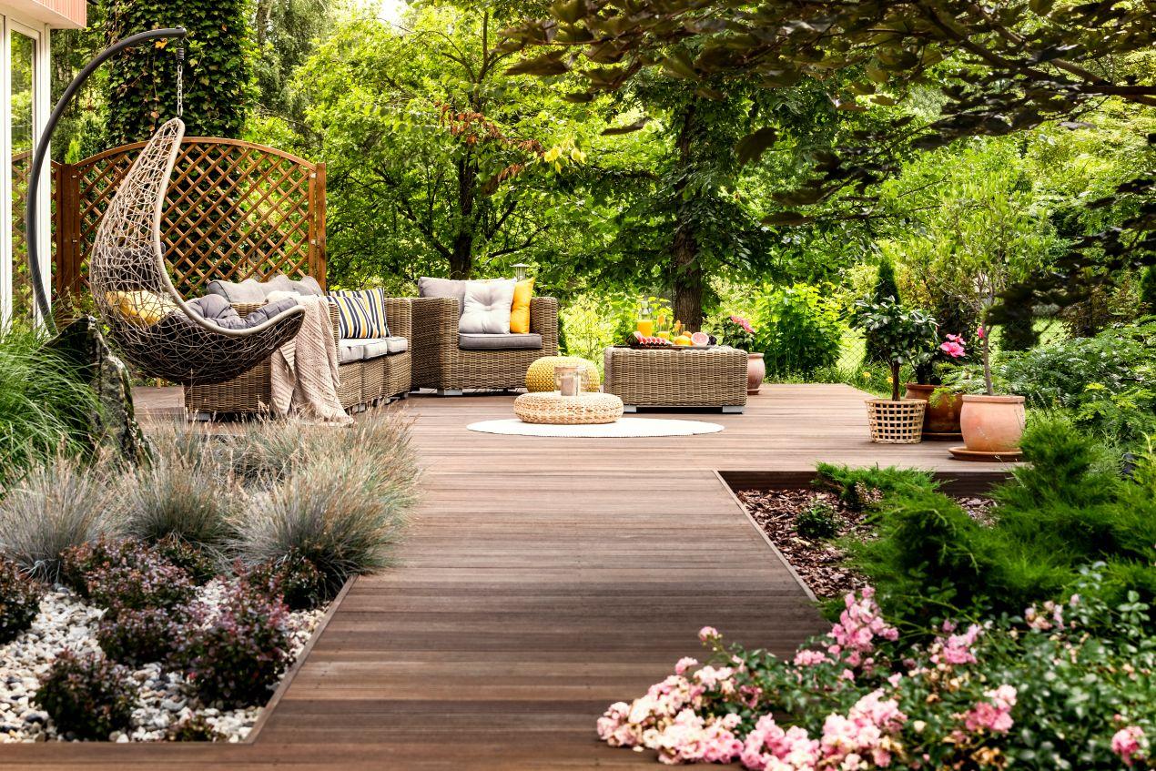 Moderne Holzterrasse mit Rattansofa und dekorativem Gartenpavillon im Hintergrund – perfekte Kulisse für stilvolle Gartenpavillons.