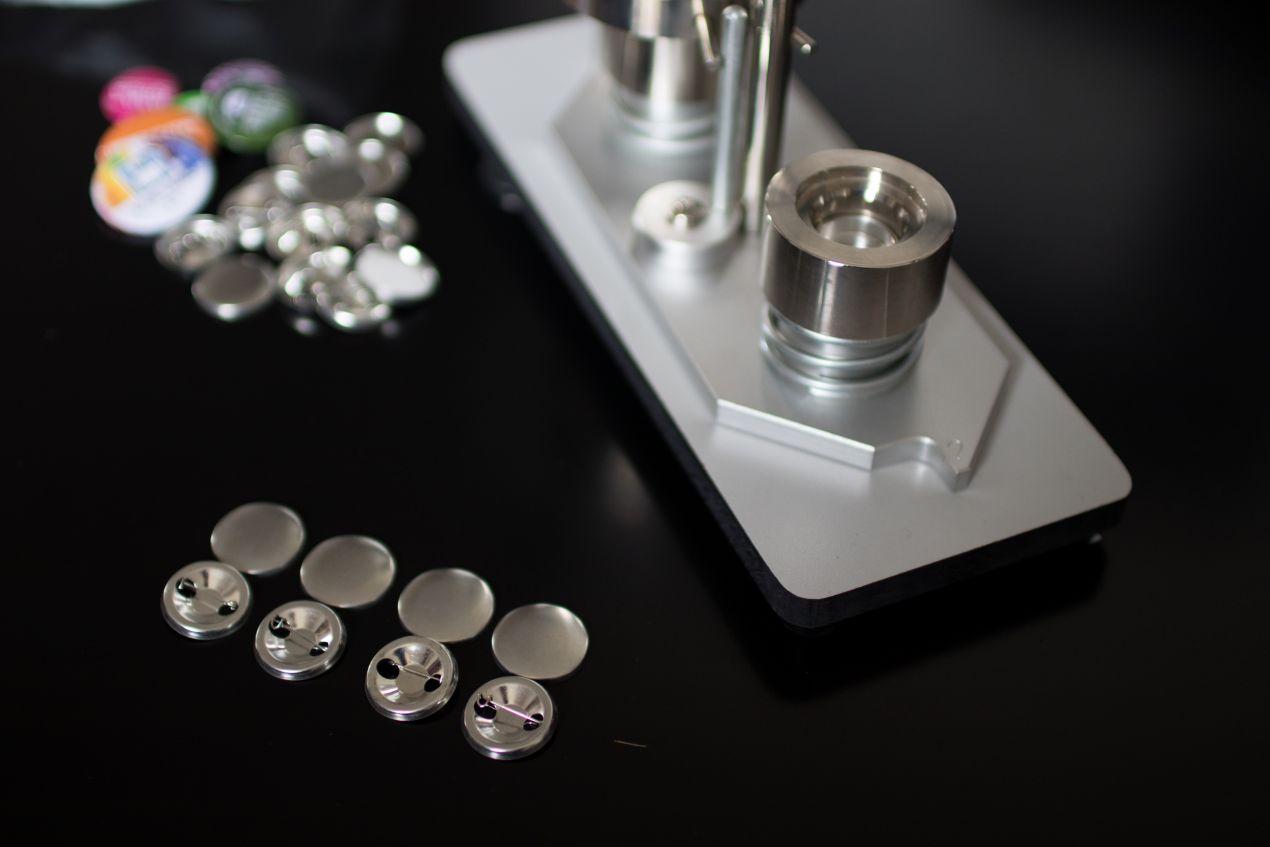 buttons selbst gestalten mit professioneller Buttonmaschine und silbernen Rohlingen auf schwarzem Tisch