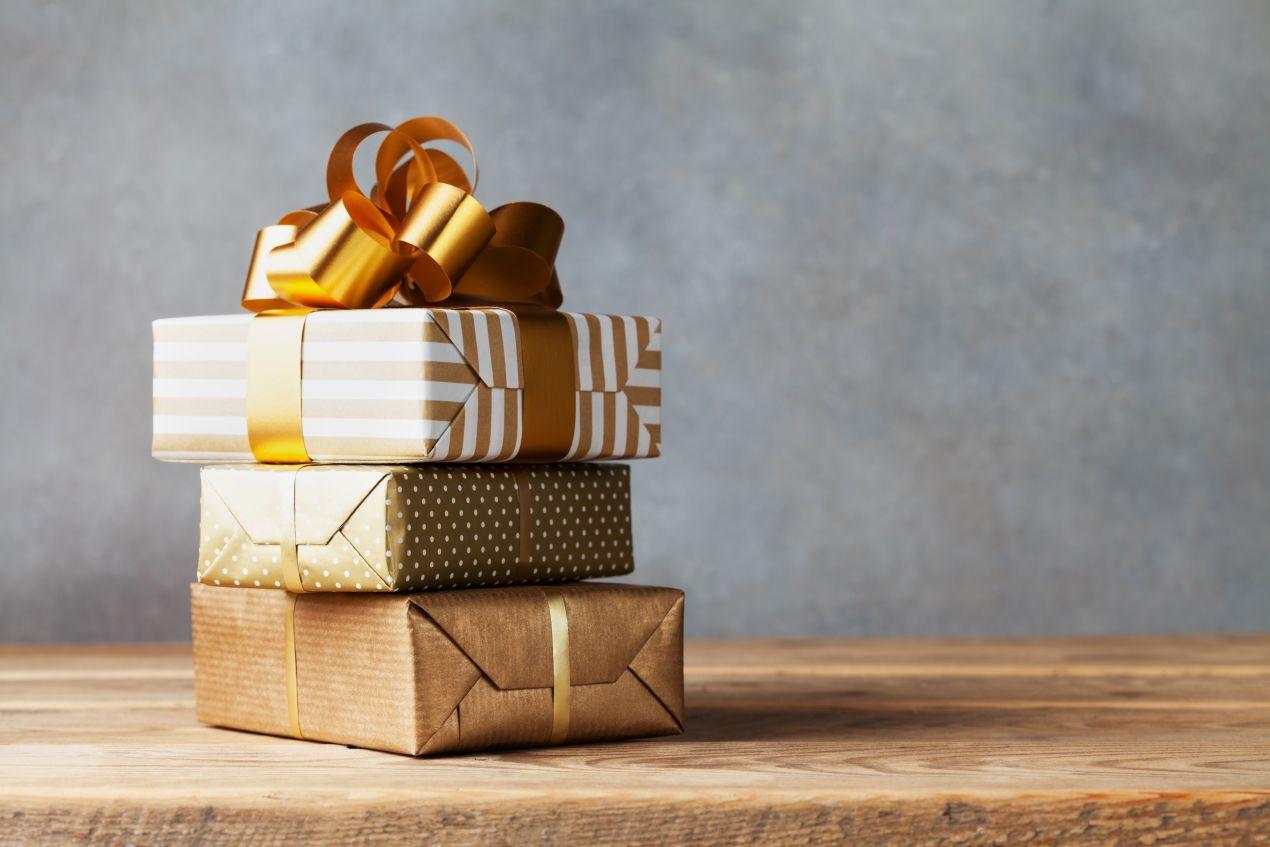 Drei elegant verpackte Geschenke mit goldener Schleife auf Holzuntergrund – ideal als Geschenkverpackung für ein Handtuch mit Namen