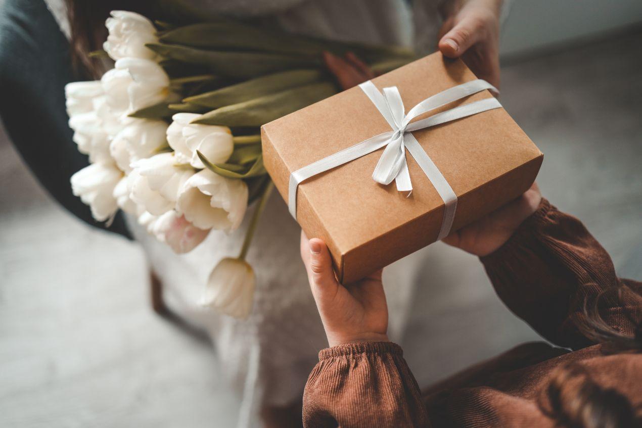 Geschenk mit weißer Schleife und weisse Tulpen in den Haenden – perfekte Szene für die Uebergabe eines Handtuchs mit Namen