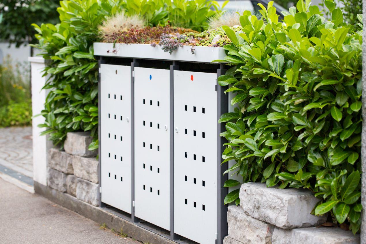 Begrünte Mülltonnenbox Metall eingebettet zwischen Hecke und Steinmauer im gepflegten Außenbereich